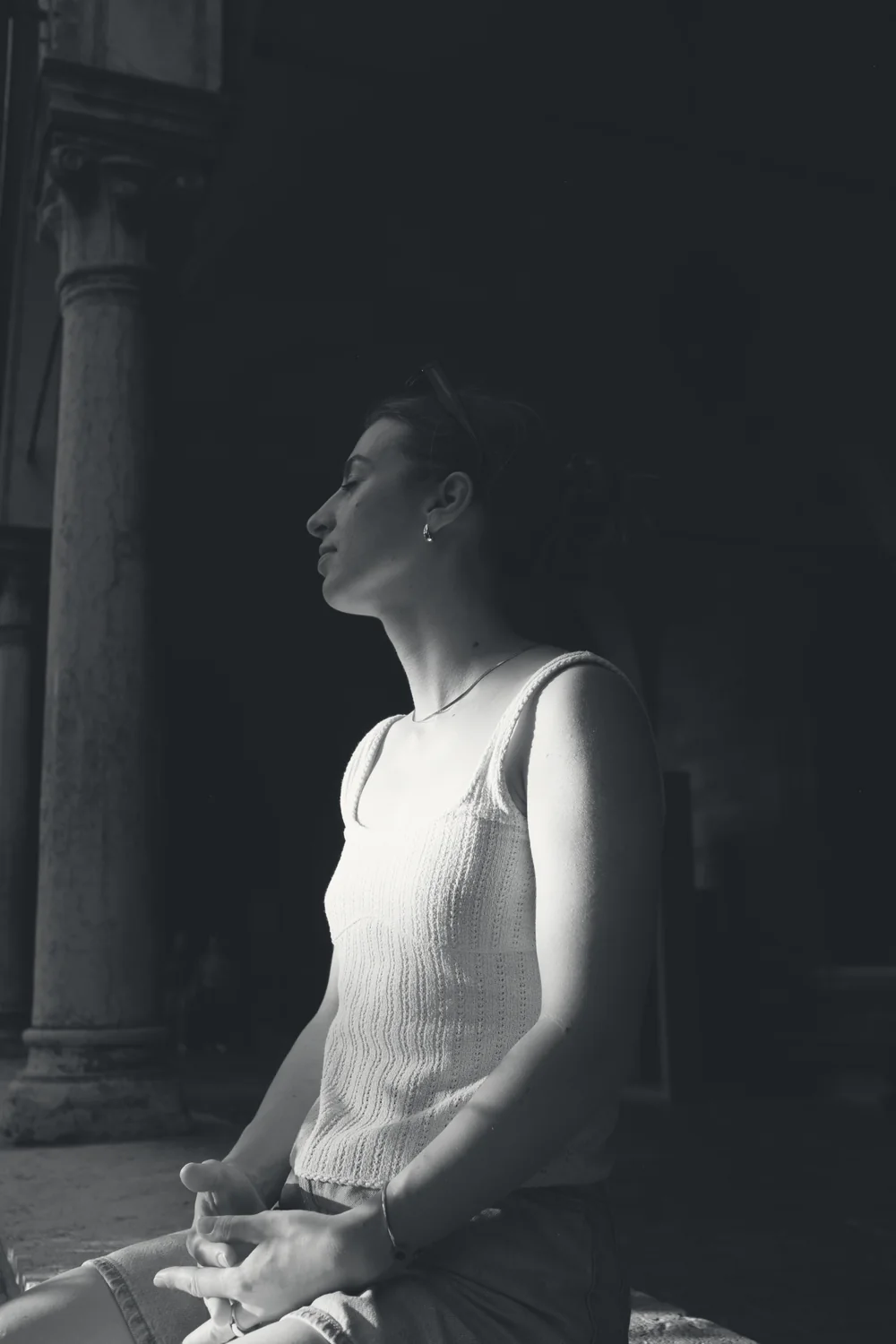 Lada Leidmane in profile with her eyes closed, sitting in the sun beside an old stone column.
